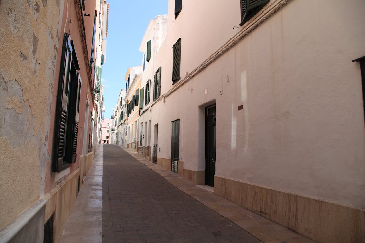 Quaint narrow street with traditional buildings in Ciudadela de Menorca, under a clear blue sky.